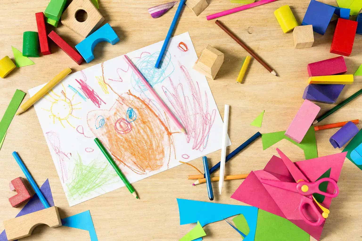 Bastel-Tisch einer Kita von oben mit Stiften, Kinderzeichnung und Bauklötzen.